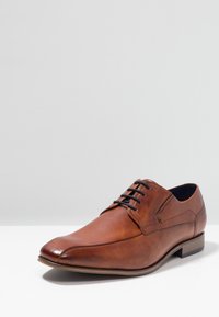 Chaussure en cuir brun à lacets avec un bout pointu, des bords arrondis et une surface texturée. Présente une couture subtile et une semelle contrastante.