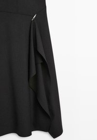 Schwarze knielange Skirt mit fließendem Design, ausgestattet mit einer drapierten Seite und einem silbernen Akzent. Hergestellt aus einem glatten, strukturierten Stoff.