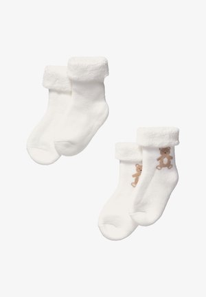 Chaussettes blanches avec un bord doux et duveteux. Une paire présente un motif d'ours brodé en beige. Les deux paires sont fabriquées dans un matériau chaud et texturé.