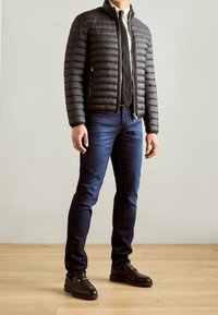 Sort dynejakke med høj krave, kombineret med mørkeblå jeans og sorte mokkasinstil sko. Jakken har lynlåslommer.