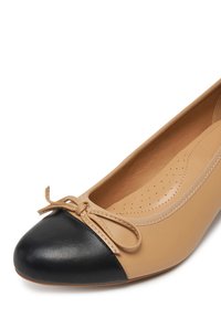 Bailarina de piel beige con una puntera redondeada en negro y un lazo en la parte delantera; textura suave con plantilla perforada.