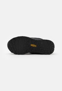 Zwarte rubberen buitenzool met een robuust profiel. Kenmerkt zich door een prominente gele logo en een gestructureerd oppervlak voor grip.