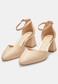 Beiga ankelbandsskor med klack, spetstå, slät läderöverkänning och en måttlig fyrkantig klack för stabilitet.