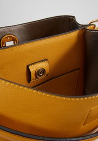 Interior de un bolso de mano de cuero amarillo con una textura suave, que cuenta con un cierre a presión y un bolsillo lateral. El forro es de un gris más oscuro.