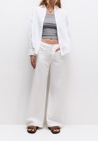 Chemise en lin blanche, débardeur gris raccourci, pantalon large blanc et tongs marron. Coupe ample avec des boutons sur la chemise et une texture minimale.
