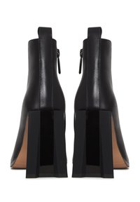 Paire de bottines en cuir noir à talons carrés, avec fermetures éclair latérales et languettes à l'arrière, vues de dos sur un fond blanc.