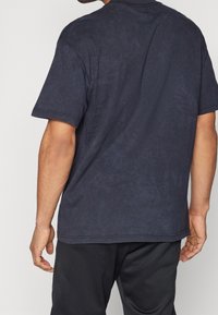 T-shirt en coton bleu marine foncé avec une coupe décontractée, des manches courtes et une texture lisse. Il présente un col rond et des détails de couture minimaux.