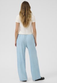 Pantaloni a gamba larga di colore azzurro chiaro con vita elasticizzata, realizzati in un tessuto morbido e liscio, caratterizzati da un design semplice e pulito. Sono visibili delle scarpe nere.