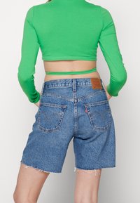 Niebieskie szorty dżinsowe z surowym wykończeniem, z dwoma tylnymi kieszeniami i skórzaną naszywką marki w talii. W połączeniu z zielonym długim rękawem.