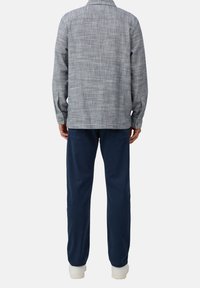 Grijs geruit shirt met lange mouwen, knoopmanchetten en een rugpas, gecombineerd met donkerblauwe broek en witte sneakers.