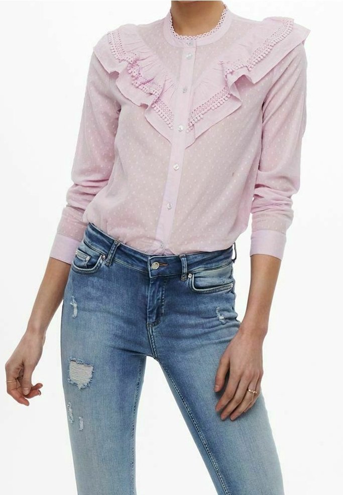 Blusa rosa chiaro con colletto arricciato, chiusura a bottoni e fantasia a pois. Abbinata a jeans blu strappati con dettagli di strappi.