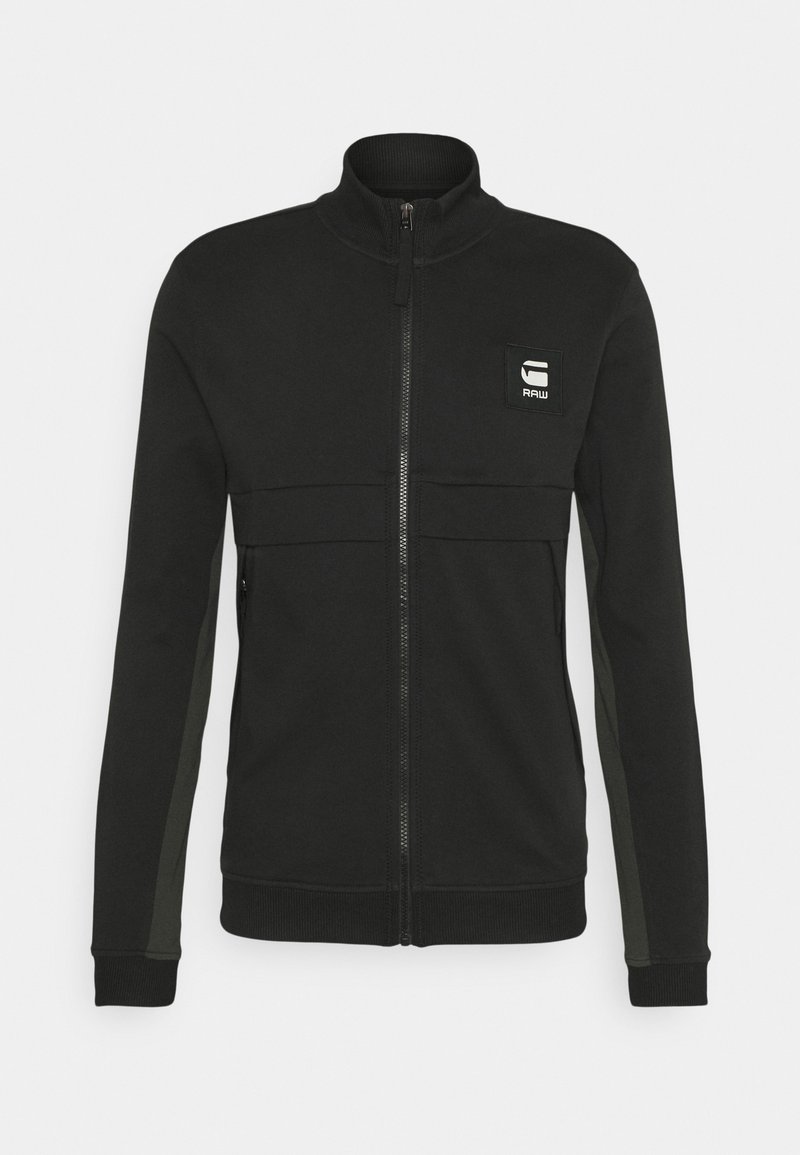 Veste noire zippée intégrale avec col, poignets et bas côtelés, poches latérales et petit patch logo blanc sur la poitrine gauche.