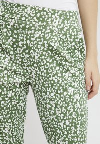 Groene broek met een wit abstract panterpatroon, voorzien van een soepele textuur en zijzakken, ontworpen met een aangesloten pasvorm bij de taille.