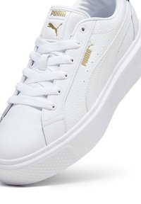 Weiße Puma-Sneaker mit strukturiertem Obermaterial, goldenen Akzenten und einer dicken weißen Sohle. Sie sind mit sechs Ösen Schnürsenkeln und einem gepolsterten Kragen ausgestattet.