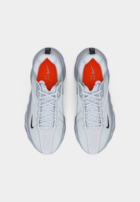 Ζευγάρι λευκά αθλητικά παπούτσια Nike με μαύρα λογότυπα swoosh, γκρι σόλες και φωτεινές πορτοκαλί εσωτερικές σόλες, εμφανιζόμενα από πάνω.