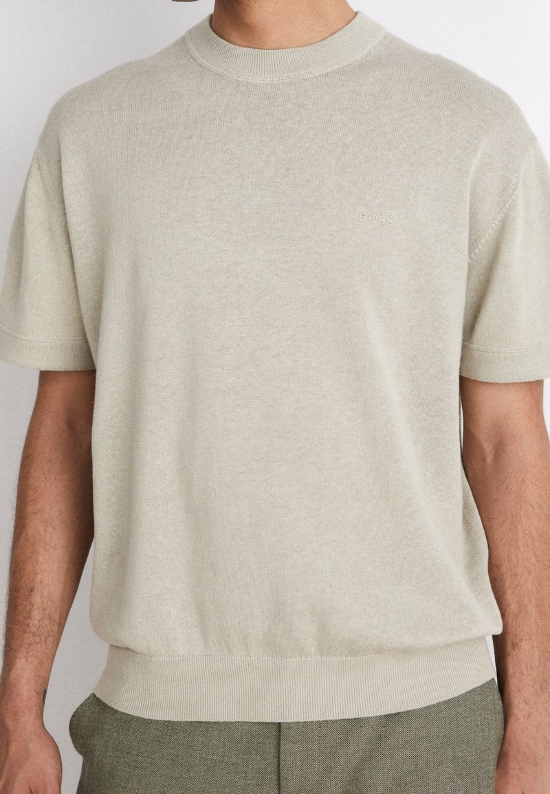 Pull en tricot beige clair avec col rond, manches courtes et ourlet côtelé. Logo "BOSS" subtil brodé sur la poitrine gauche.