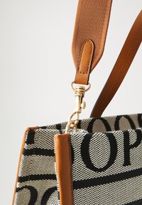 Sac en toile avec un motif tissé noir et crème, présentant des accents en cuir marron et un fermoir doré pour l'attache de la bandoulière.