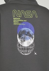 Logo et texte de la NASA sur un hoodie sombre avec graphique de lune bleu et blanc et globe filaire blanc sous le texte.