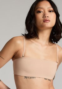 Huidskleurige bralette met een zachte, rekbare textuur, voorzien van dunne verstelbare bandjes en een minimalistisch ontwerp dat eenvoud benadrukt.