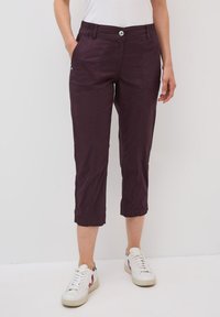 Pantaloni cropped viola con vita elasticizzata e tasche laterali. Tessuto morbido con un leggero lucido. Indossati con sneaker bianche.
