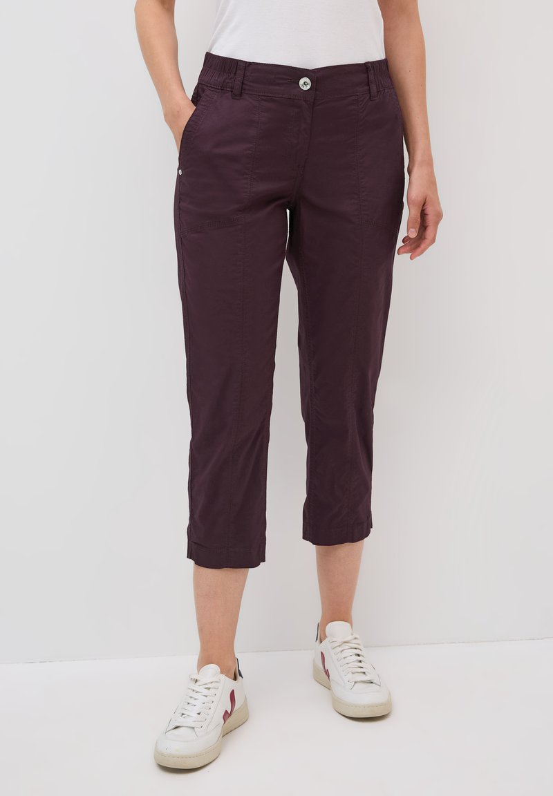 Pantaloni cropped viola con vita elasticizzata e tasche laterali. Tessuto morbido con un leggero lucido. Indossati con sneaker bianche.