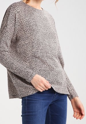 Langarmshirt aus hellbeigem Stoff mit schwarzem Sternmuster, mit lockerer Passform und abgerundetem Saum, kombiniert mit blauen Jeans.