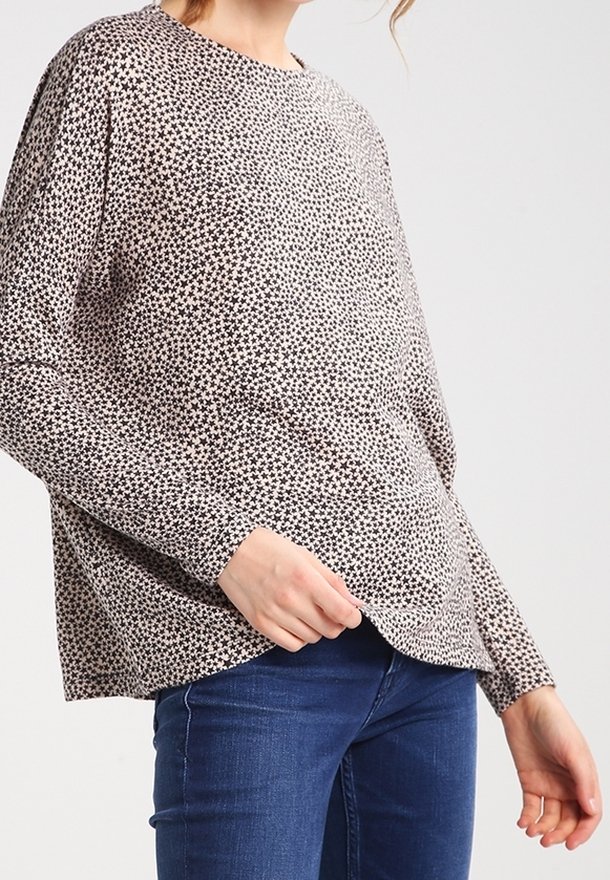 Langarmshirt aus hellbeigem Stoff mit schwarzem Sternmuster, mit lockerer Passform und abgerundetem Saum, kombiniert mit blauen Jeans.