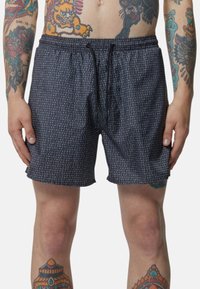 Costume da bagno neri con un motivo di testo bianco ripetuto, vita elastica e lacci. Tessuto leggero, lunghezza sopra il ginocchio.