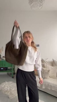 Jauna sieviete ar blondiem matiem tur lielu tumši brūnu somu gaišā dzīvojamā istabā ar baltu dīvānu un zaļu skapi.