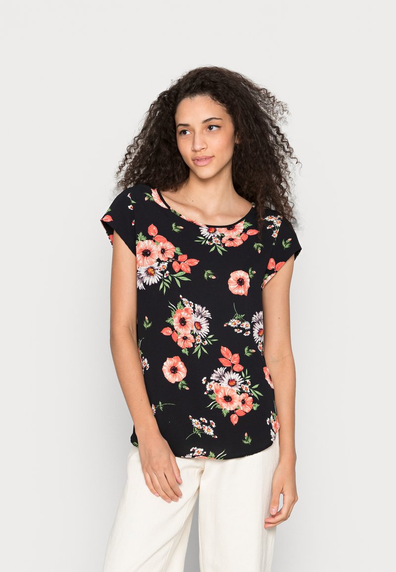 Top preto com padrão floral, apresentando mangas curtas, um decote redondo, flores vibrantes em coral e branco, com um corte descontraído. Combinado com calças de tom claro.