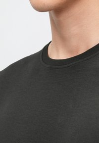 Črna bombažna majica s krožnim izrezom, gladke teksture, brez vidnih vzorcev ali grafičnih motivov, prikazana iz bočnega kota.