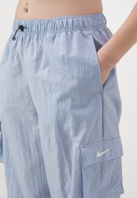 Světle modré, lehké cargo šortky s elastickým pasem, bočními kapsami a malým bílým logem Nike na cargo kapse.