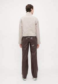 Light gray cropped jacket with a high collar, paired with brown pleather wide-leg pants, featuring a smooth texture and minimalist design.