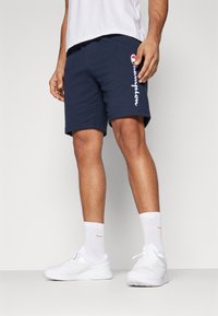 Pantalones cortos deportivos de la Marina con el logo blanco de "Champion", fabricados en tejido suave, combinados con zapatillas blancas y calcetines de caña baja. Diseño simple, cinturilla elástica.