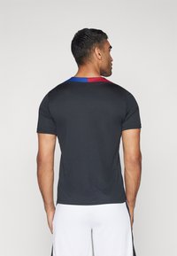 Sort atletisk T-shirt med tekstureret stof, der har en farvet accent ved kraven i blå og rød. Korte ærmer, tætsiddende design.