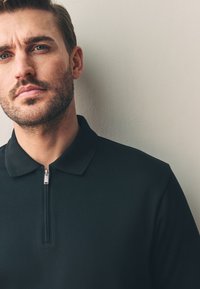 Zwart poloshirt met een kraag met rits, gemaakt van gladde stof, met een getailleerd ontwerp en een subtiele textuur op het oppervlak.