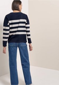 Marineblau gestreiftes langärmliges Oberteil mit cremefarbenen horizontalen Streifen. Kombiniert mit hellblauen gerade geschnittenen Jeans. Einfaches Design und lässige Passform.
