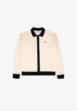 Cremefarvet strikket cardigan med knapper, sort krave, manchetter, kant og et lille "obey"-logo på venstre bryst.
