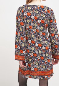 Robe à impression florale avec des manches longues, présentant des fleurs orange, jaunes et blanches sur fond marine ; tissu texturé avec un ourlet à motifs.