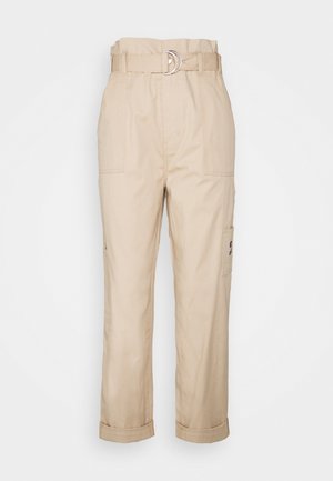 Beżowe spodnie cargo o luźnym kroju, z szerokim paskiem z srebrną klamrą w kształcie litery D, dwoma przednimi kieszeniami i podwiniętymi mankietami.