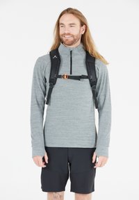 Szary długi sweter z zamkiem na szyi, połączony z czarnymi szortami. Noszony z czarnym plecakiem z pomarańczowym zapięciem.