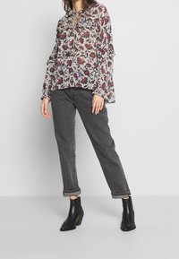 Blouse à manches longues florale avec des poignets volantés en crème, rouge et bleu, associée à un jean gris avec ourlets retroussés et des bottines noires.