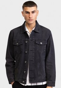 Zwarte denim jack met twee borstzakken, zilverkleurige hardware en een klassieke kraag. Heeft een knoopsluiting aan de voorkant en een relaxte pasvorm.