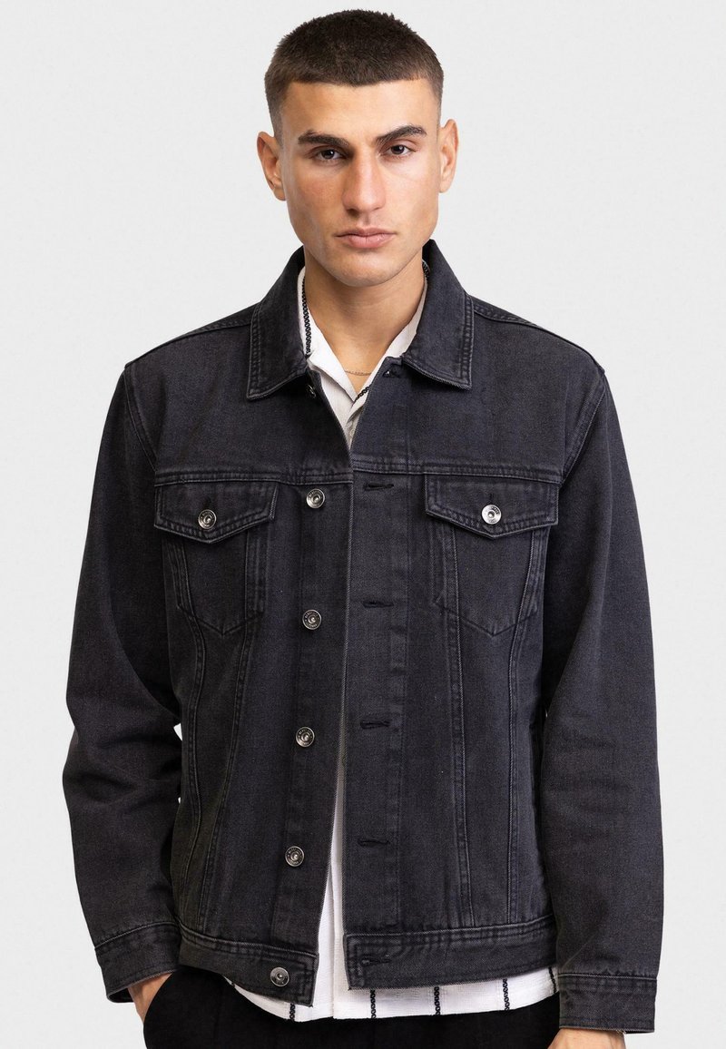 Zwarte denim jack met twee borstzakken, zilverkleurige hardware en een klassieke kraag. Heeft een knoopsluiting aan de voorkant en een relaxte pasvorm.