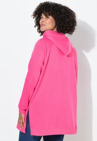 Růžová mikina s kapucí s volným střihem, bočními rozparky a dlouhými rukávy, vyrobená z měkké látky a s jednoduchým designem.