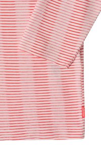 Hvidt stof med tynde, horisontale røde striber og en langærmet model, der har en lille rød mærkat med teksten "STEADY" på sidesømmen.