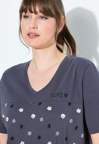 T-shirt grigia a V con motivo floreale in nero, bianco e blu. Presenta la scritta "LOVE" ricamata sopra il design. Tessuto morbido.