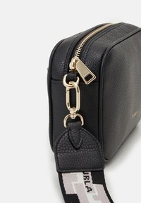 Černá kožená taška s hrubou texturou, zlatým zipem a kováním. Má vzorovaný nastavitelný popruh. Hladký obdélníkový design.