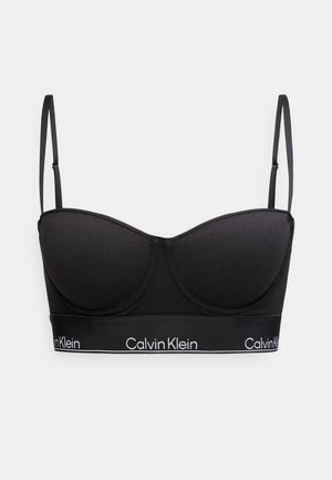 Must Calvin Kleini polsterdatud rinnahoidja reguleeritavate õhukeste rihmade ja kaubamärgiga elastse alaosa ribaga ühtlasel taustal.