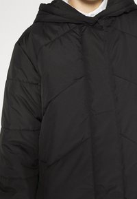 Black puffer jacket with a hood, featuring a quilted design and textured finish. The fabric appears smooth with diagonal stitching accents.